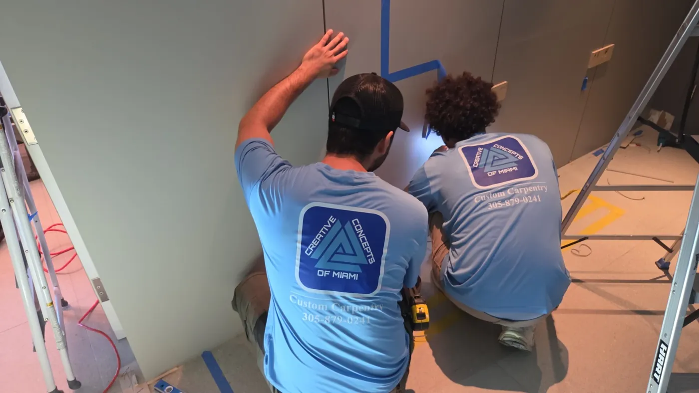 Two carpenters at work wearing light blue tees with a large printed company logo on the back